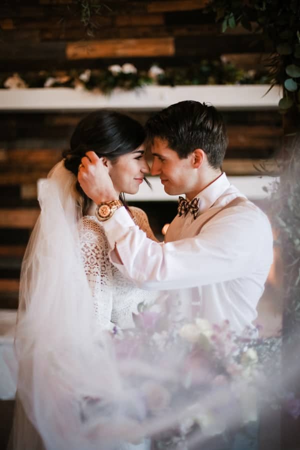 Couple with foreheads together indoors, the groom cradling the bride's head, veil framing the shot