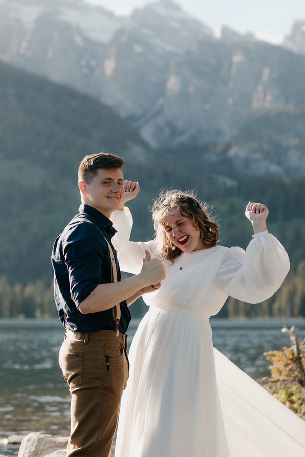 Bride and groom pumping their fists and laughing by a mountain lake
