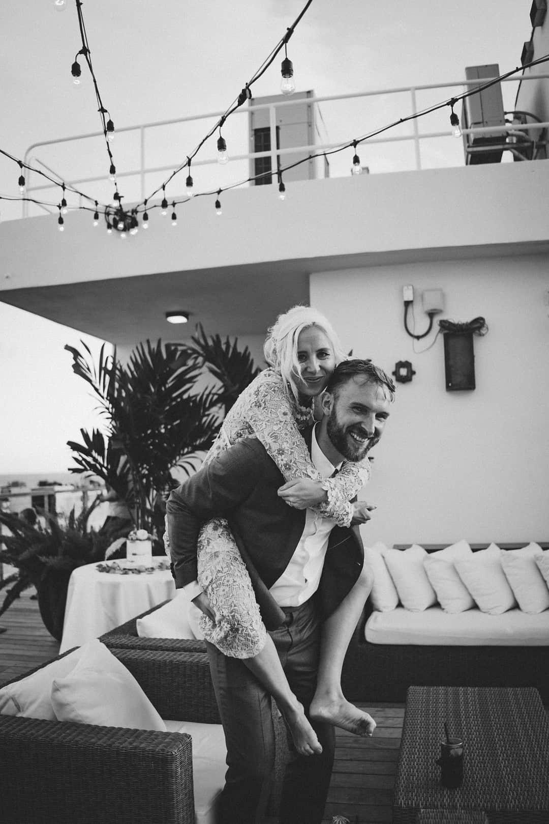 Groom giving the bride a piggyback ride on a rooftop terrace, both laughing