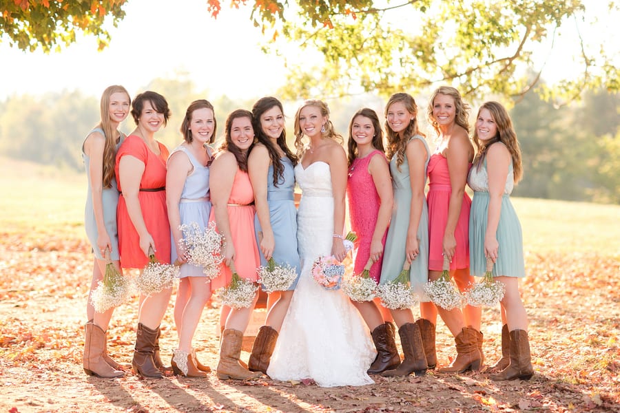 Bridesmaids in mismatched bright dresses with cowboy boots holding baby's breath