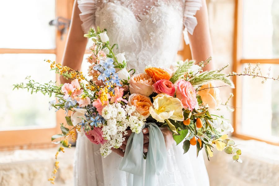 Loose bouquet with coral and pink ranunculus, peach garden roses and blue delphinium