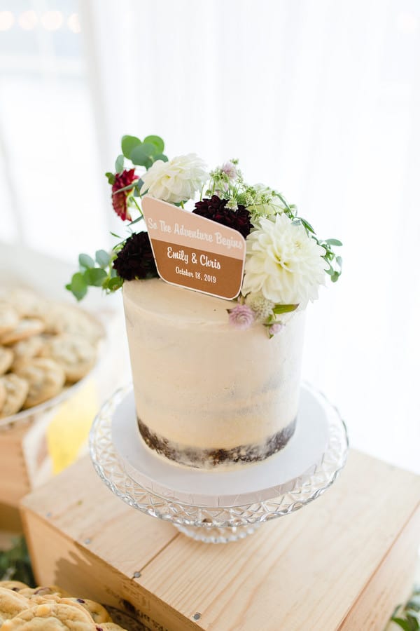Single-tier semi-naked buttercream cake with burgundy and white dahlias and a wooden October wedding date sign