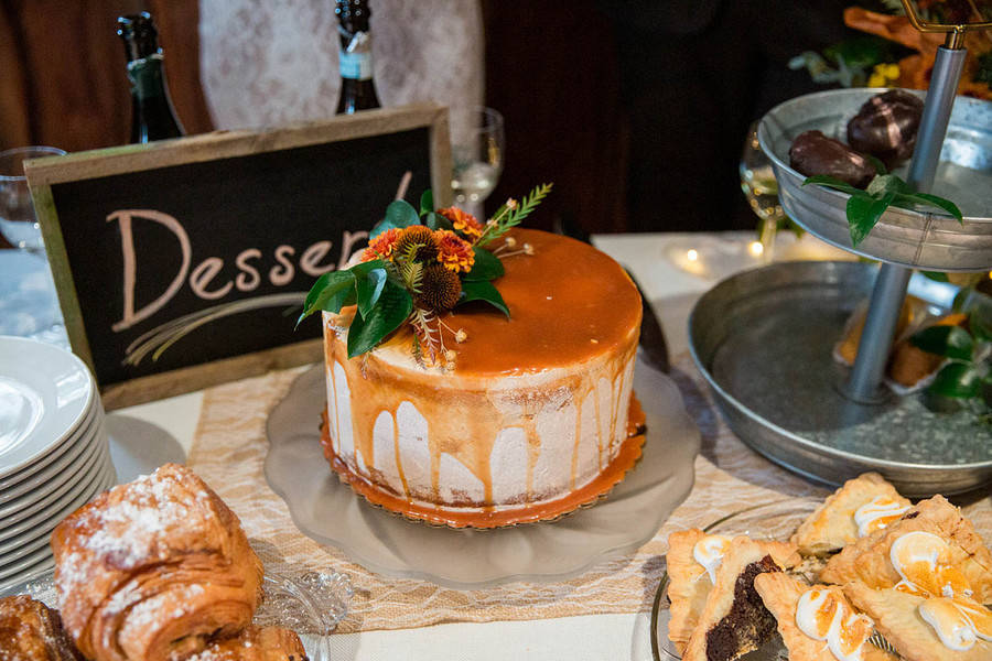 Single-tier semi-naked cake with a caramel drip and rust-colored flowers beside a Dessert chalkboard sign