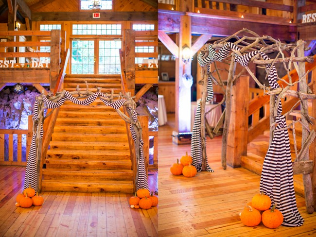 Rustic branch wedding arch wrapped in black and white striped fabric with orange pumpkins at the base