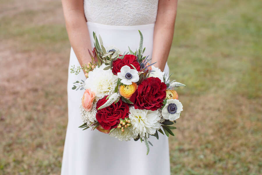 Bouquet with yellow-orange ranunculus, white anemones and deep red roses