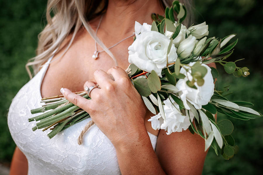Bride holding a small white ranunculus bouquet with olive greenery