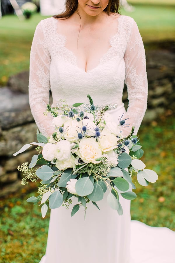 White ranunculus and garden roses with blue thistle and trailing eucalyptus