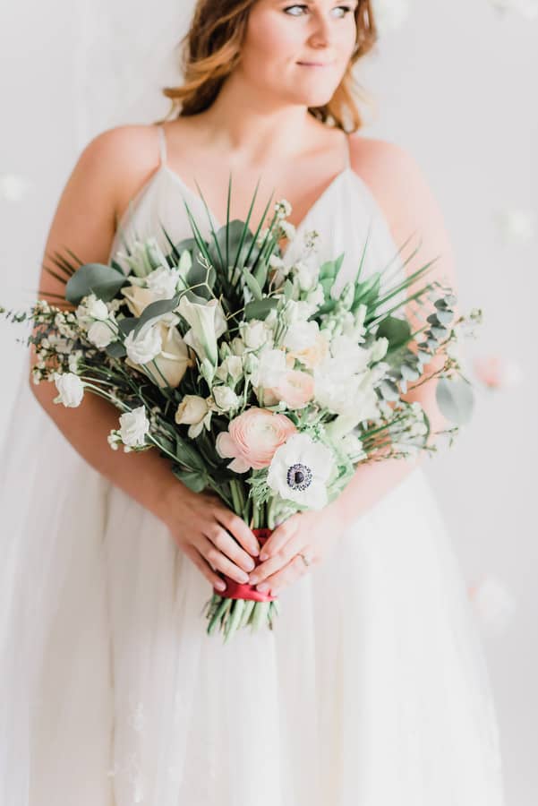 Blush pink ranunculus above a white anemone in a soft green-and-white bouquet