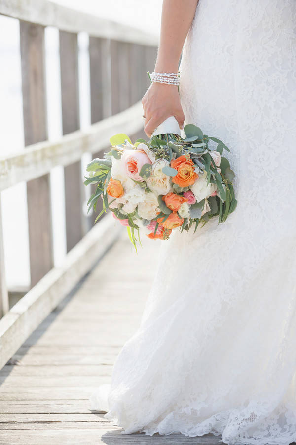 Bouquet with bright orange ranunculus, peach garden roses and white peonies by the water
