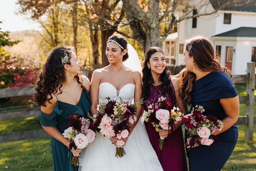 Three bridesmaids in mismatched emerald wine and navy gowns holding dahlia bouquets