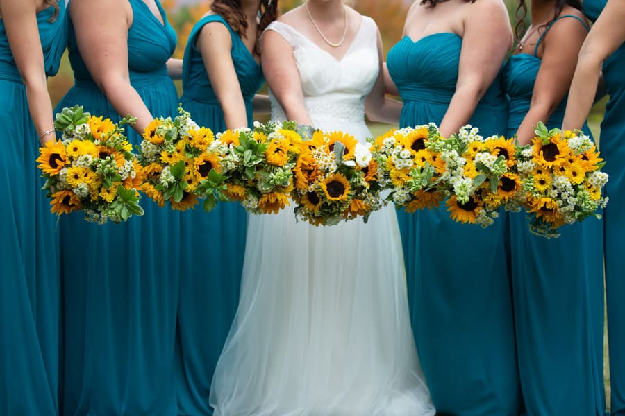 Bridesmaids in teal gowns holding sunflower bouquets