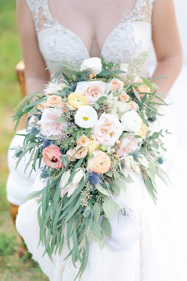 Cascading bouquet of peach, yellow and white ranunculus with blush roses and thistle