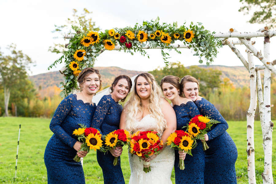 Bridesmaids in navy long-sleeve lace gowns holding sunflower and red rose bouquets