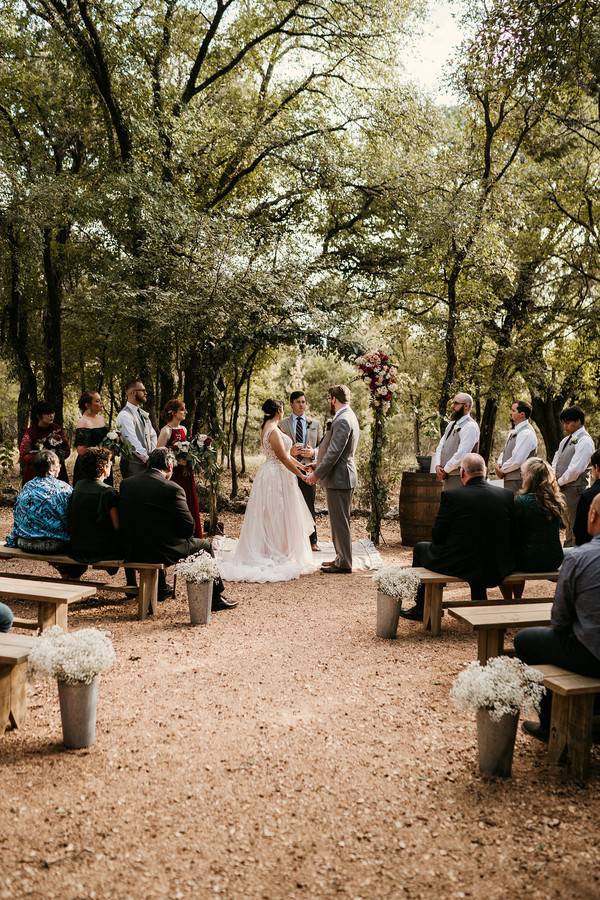 Slim metal wedding arch with a burgundy floral cluster at the top corner in an oak grove ceremony
