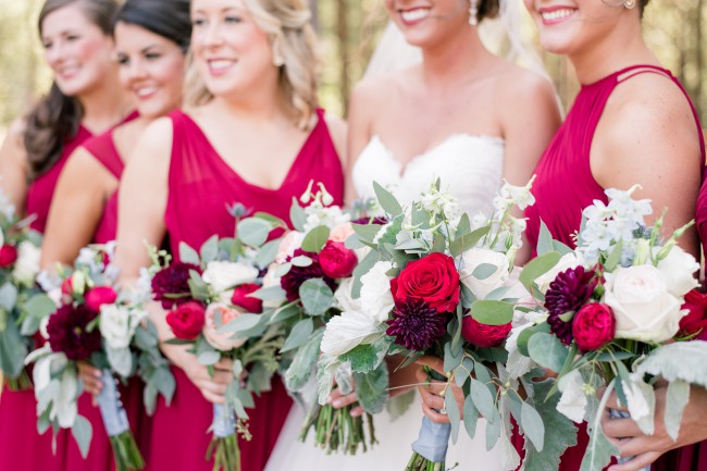 Bridesmaids in burgundy gowns holding red and white bouquets