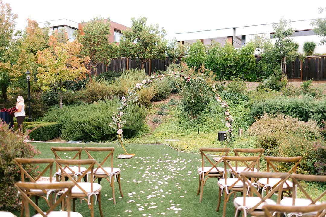 Circular wedding arch with blush and cream florals climbing one side at the end of a petal-lined aisle