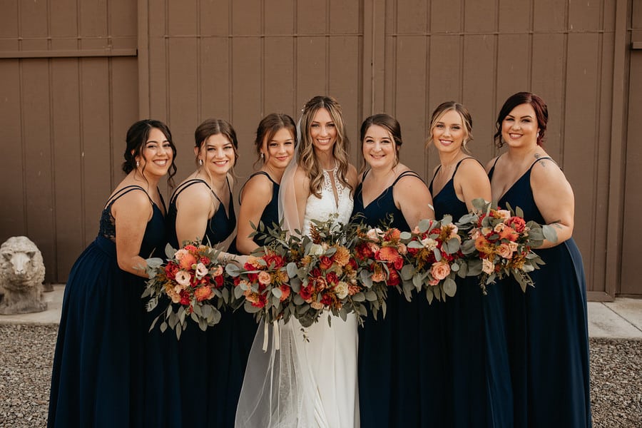 Bridesmaids in navy floor-length gowns holding rust and terracotta bouquets