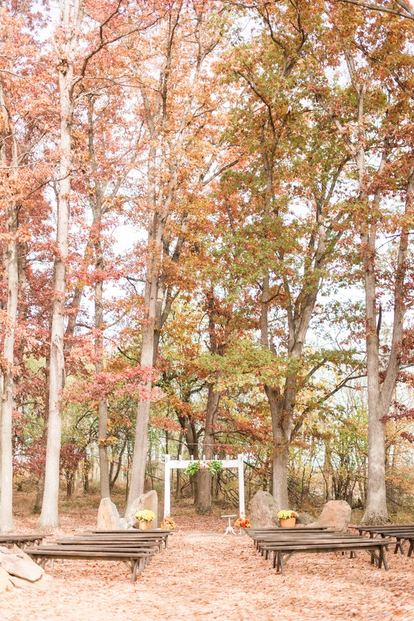 Small white wedding arch with a greenery swag in a woodland clearing surrounded by peak copper and gold fall foliage