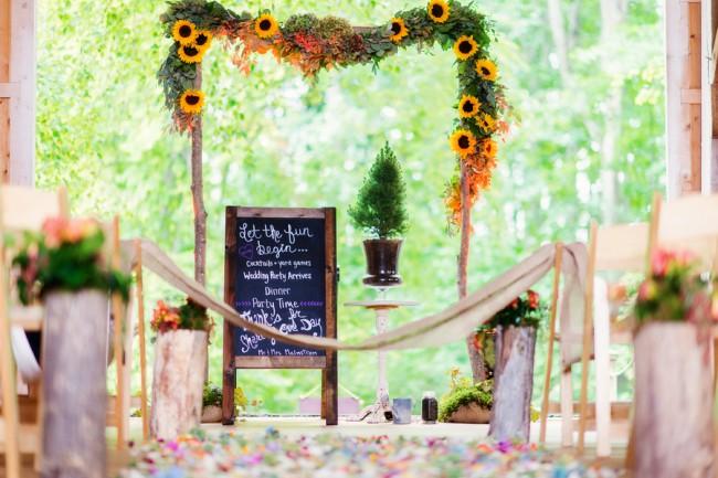 Wood canopy wedding arch with a garland of sunflowers and greenery over a chalkboard sign
