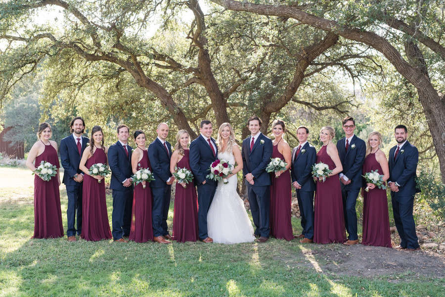 Bridal party in burgundy halter gowns under a large oak tree