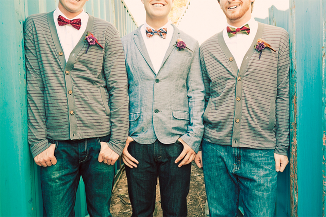 Three men in grey cardigans and a chambray blazer with patterned bow ties and dark denim jeans against a teal wall