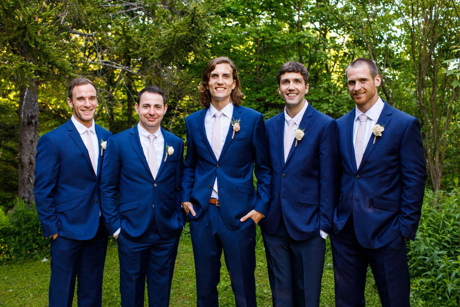 Five groomsmen in cobalt blue suits with blush pink ties and white rose boutonnieres in green woodland