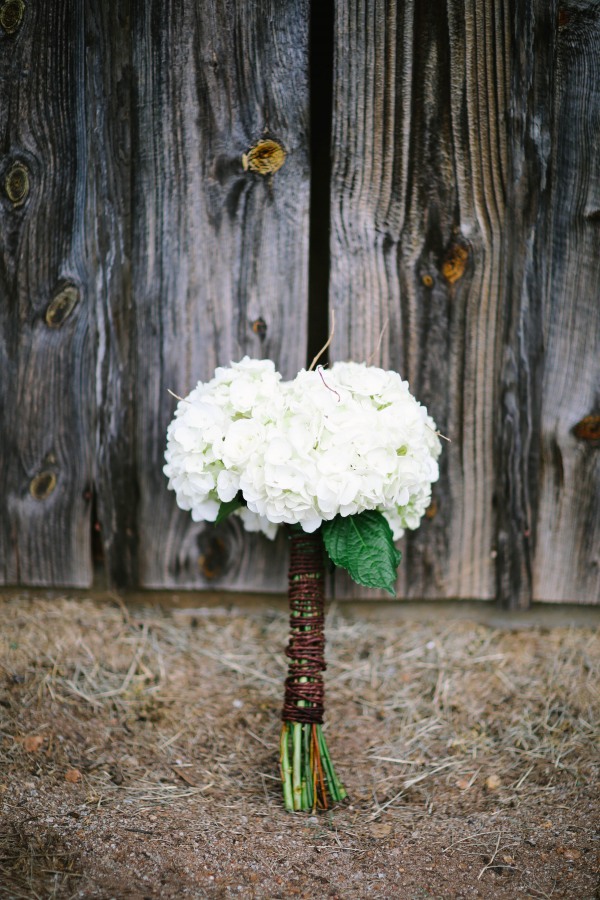 Round white hydrangea bouquet with twine-wrapped stems against weathered barn wood
