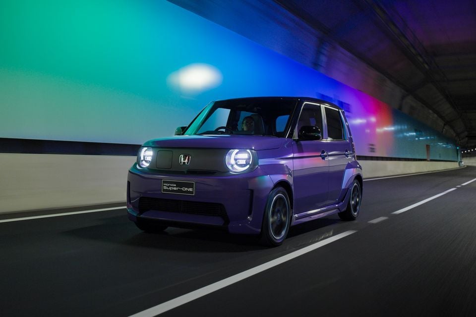 A purple Honda Super-One electric hatchback driving through a tunnel with colourful lighting at night.