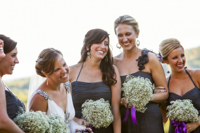 Bridesmaids in grey dresses holding all-baby's-breath bouquets tied with purple ribbon