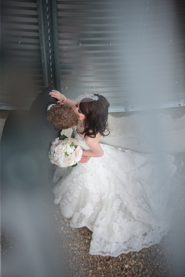 Loose round bouquet of blush and cream roses held by a bride in a lace ballgown