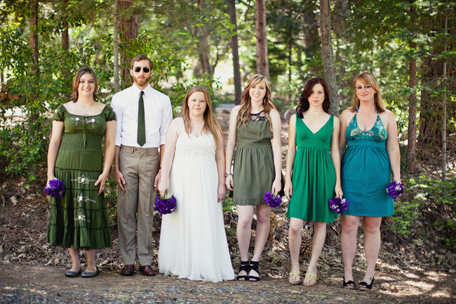 Bridal party in green dresses holding small purple posies in a forest