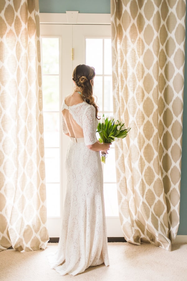 Bride holding a bunch of white tulips with long green stems by a window