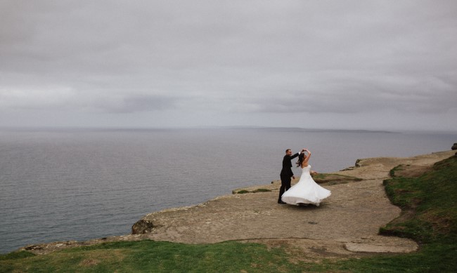 Bride and groom holding hands on the edge of the Cliffs of Moher