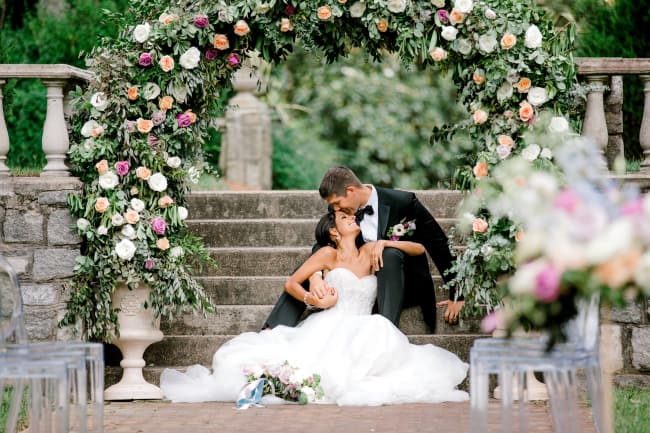 Couple beneath a lush floral ceremony arch on stone steps