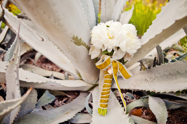 White peony bouquet with a mustard-yellow lace handle resting on an agave plant