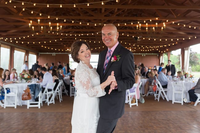 An older bride and groom sharing a slow dance under string lights at their reception, hands joined