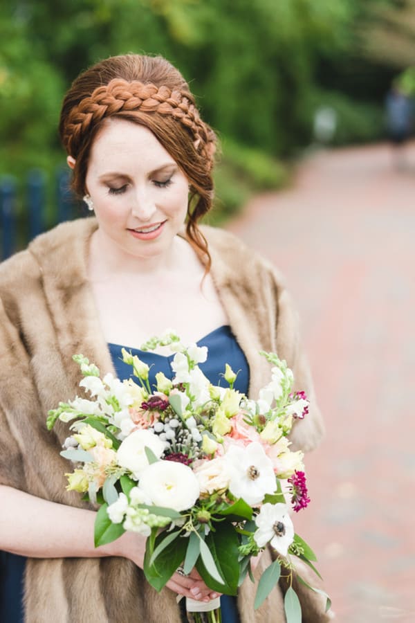 Bride in a caramel mink stole over a navy strapless gown with a crown braid, holding a pastel bouquet