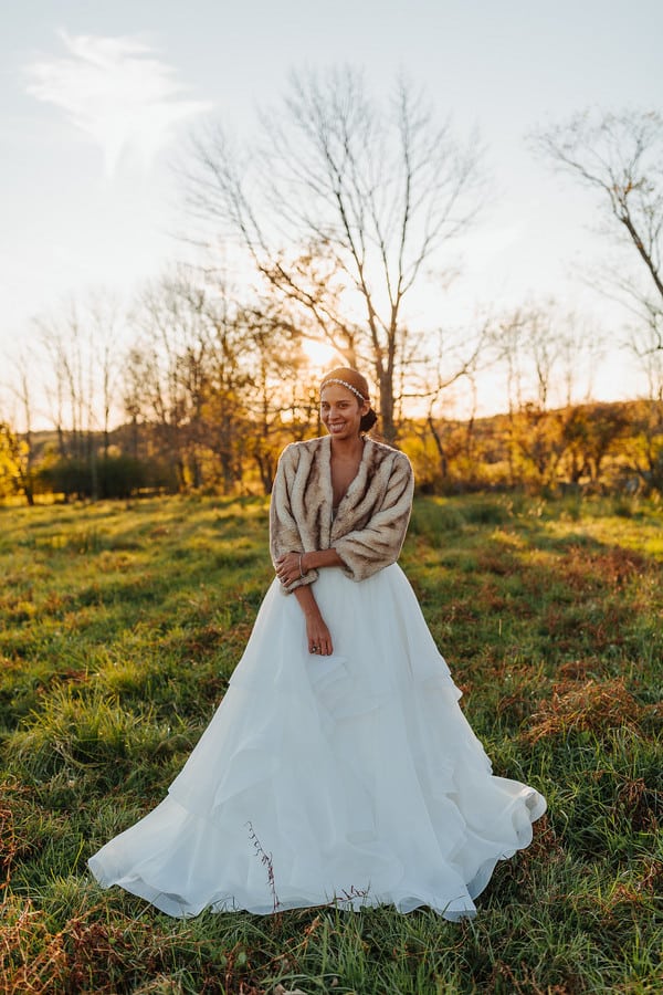 Bride in a caramel fur stole over a full tulle ballgown at golden hour with bare trees behind