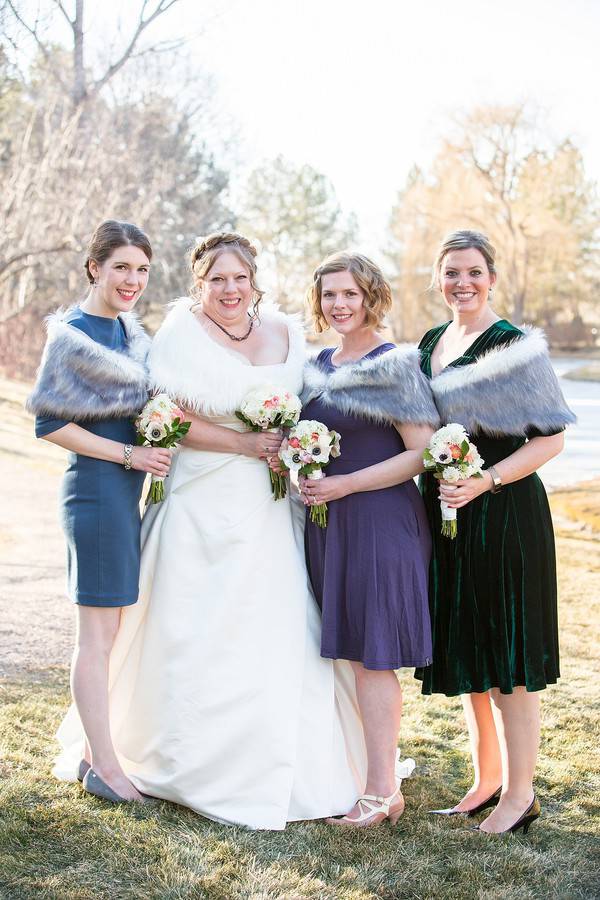 Bride in an ivory fur stole beside three bridesmaids in grey fur stoles and jewel-tone dresses