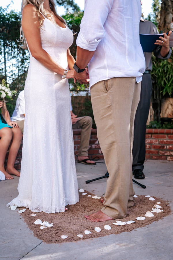 Barefoot bride and groom at a backyard beach micro-wedding altar with sand underfoot