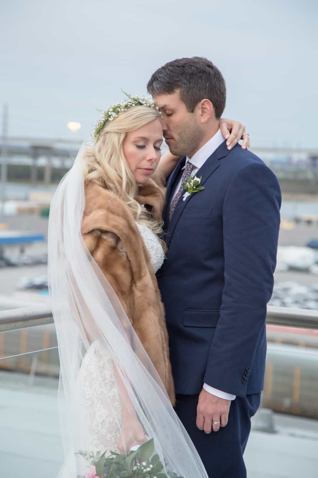 Bride in a honey mink fur coat and baby's-breath crown embracing her groom in a navy suit