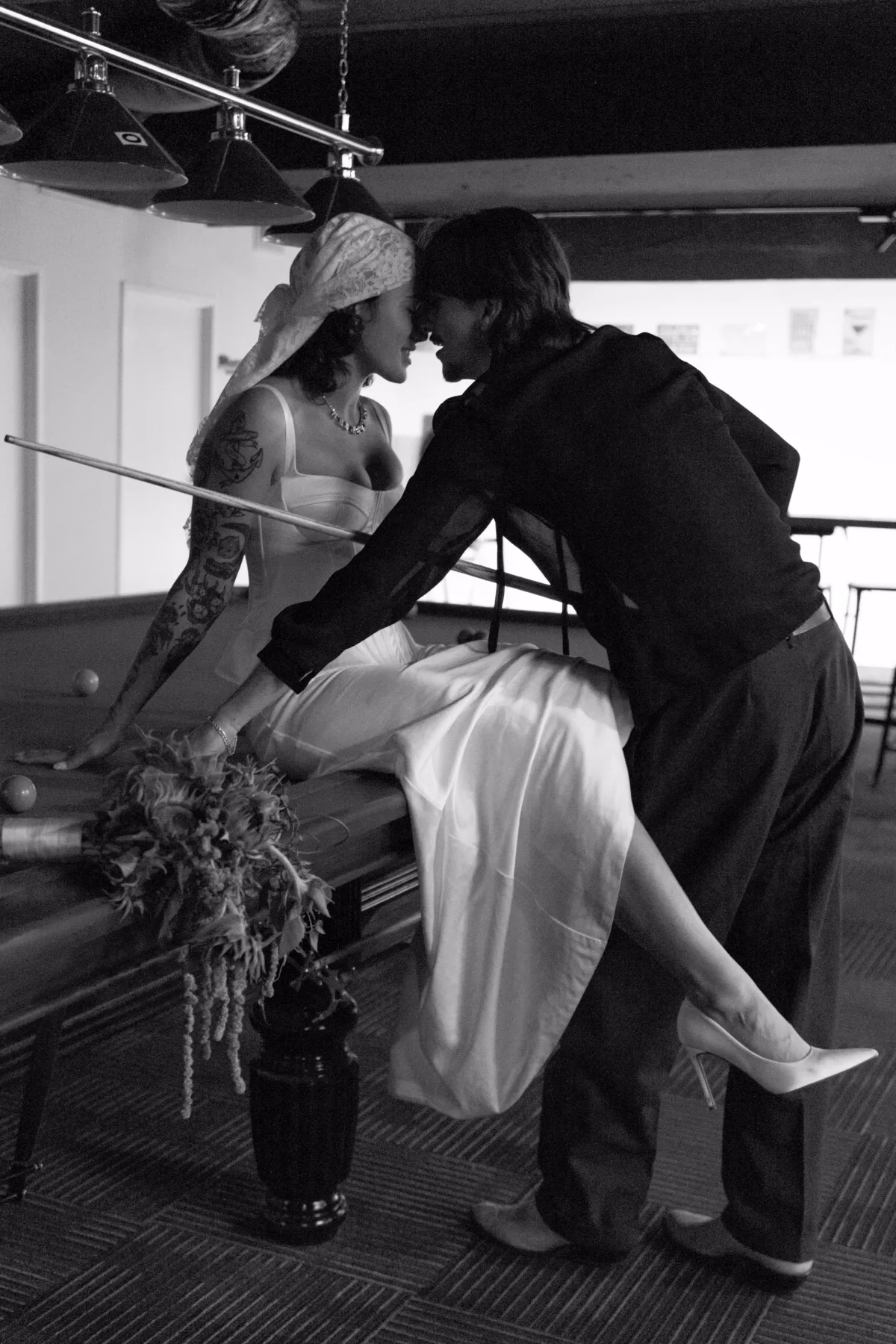 Black and white photograph of a bride in a lace headscarf laughing with the groom outside a doorway.