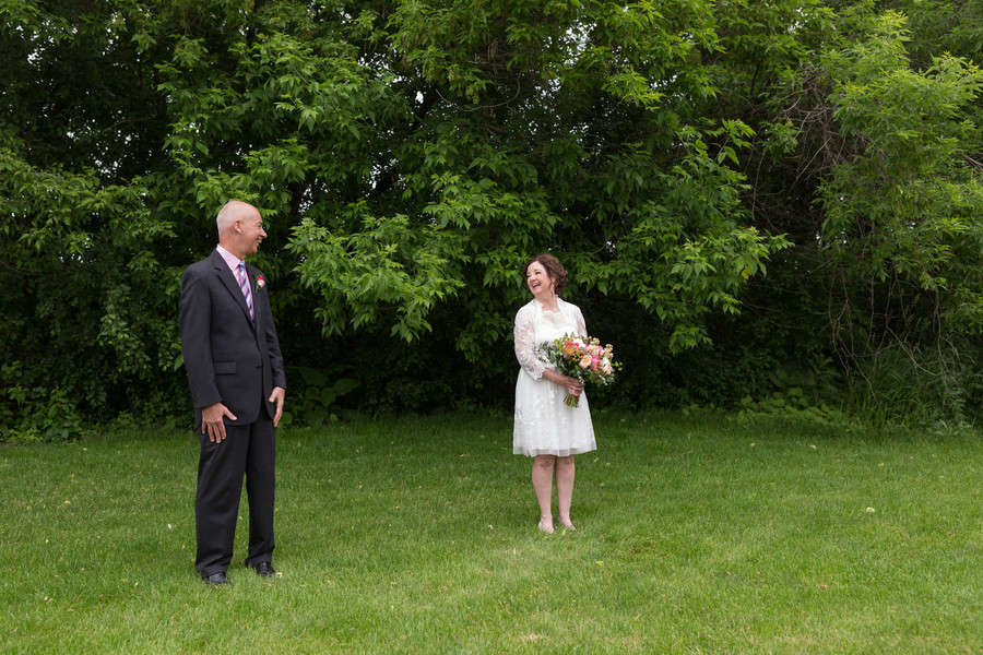 An older bride and groom standing a few feet apart on a green lawn, laughing at each other