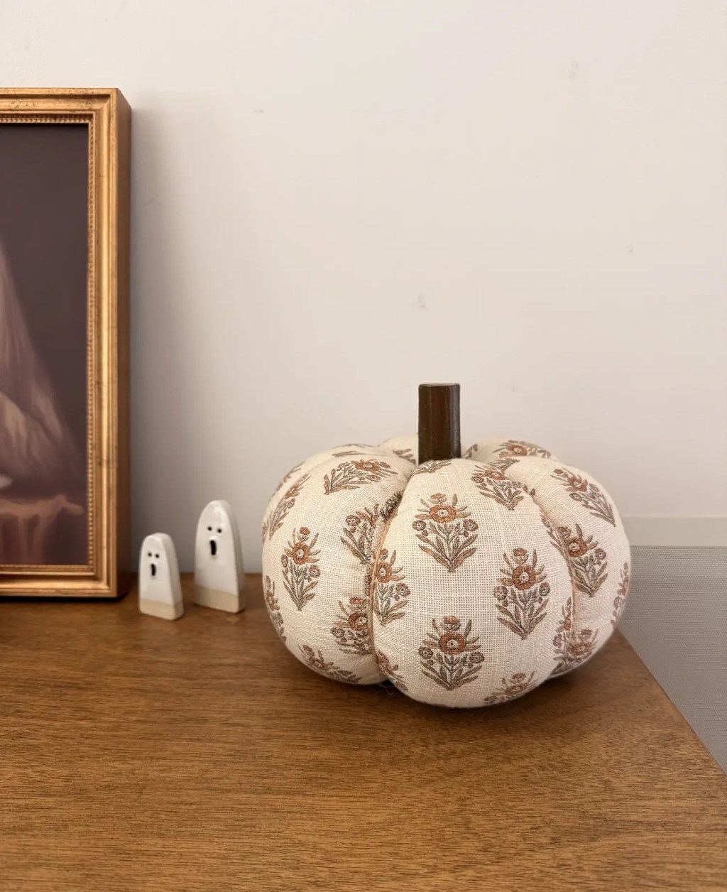 Rust and cream block print fabric pumpkin with a wood stem on an entry table beside two small ghost figurines