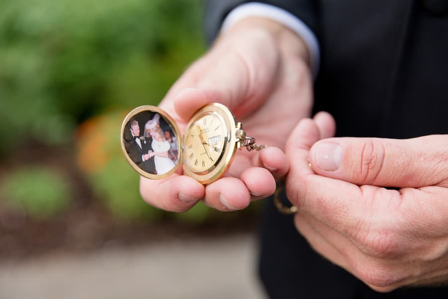 Hands holding an open gold pocket watch with a wedding photo inside the lid