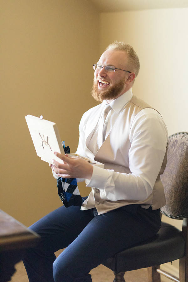 Groom laughing as he holds up an opened gift box while getting ready