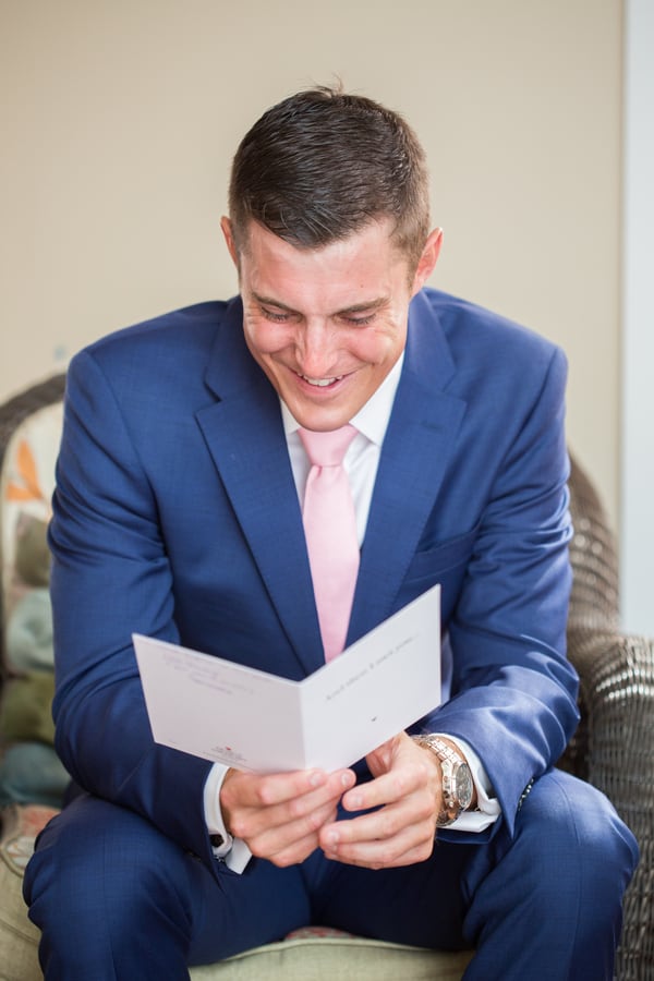 Groom in a blue suit smiling as he reads an open card