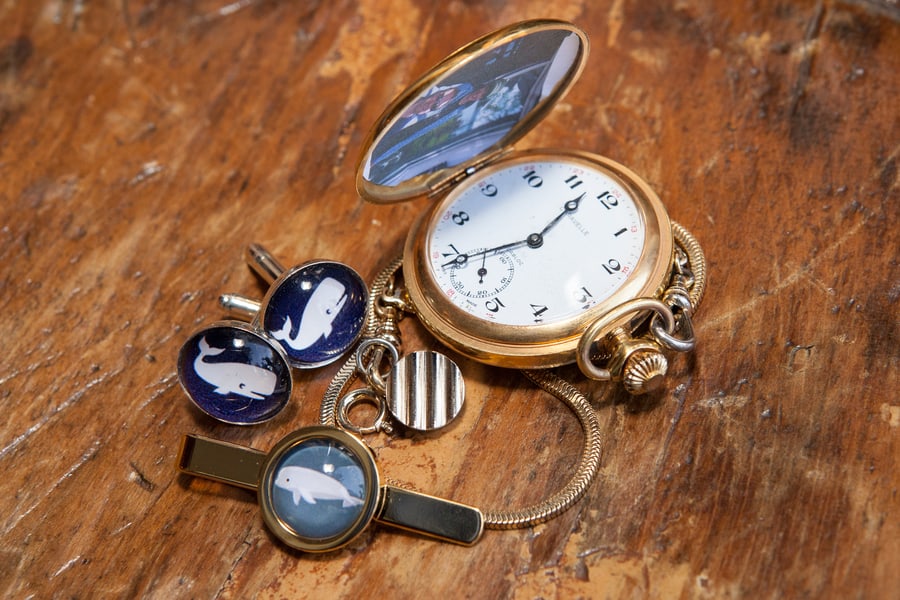 Open gold pocket watch on a chain beside whale cufflinks and a tie bar