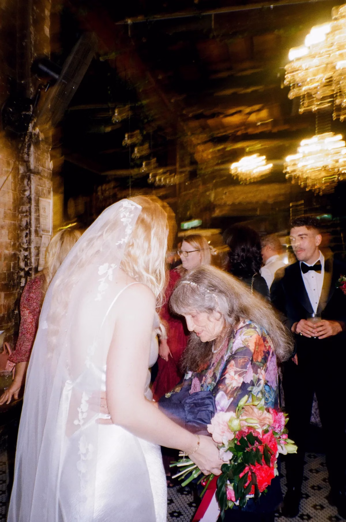 Bride leaning towards an older wedding guest in a floral outfit during the reception.