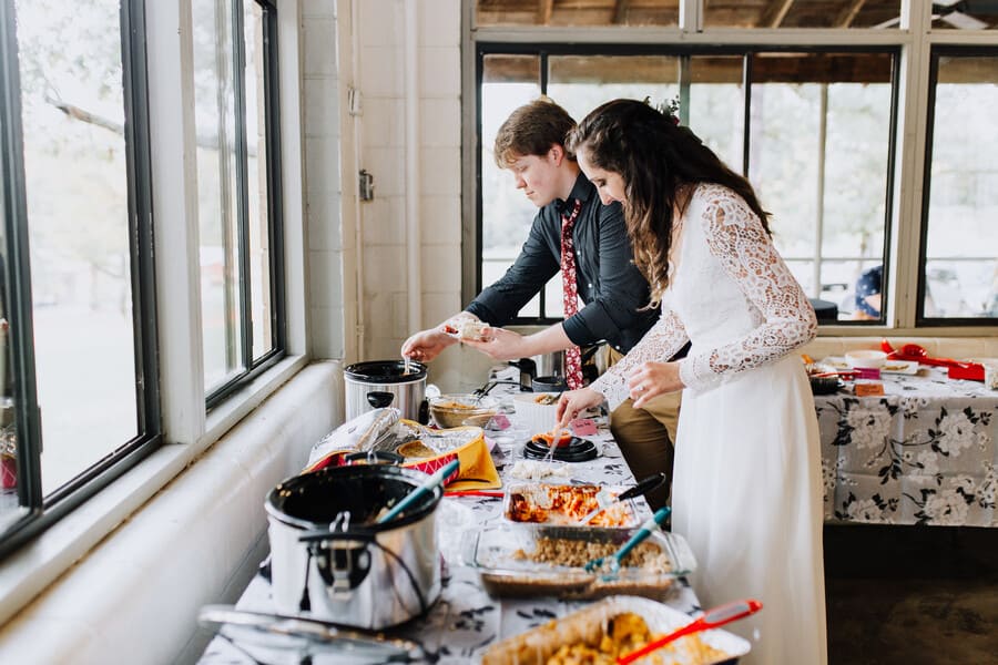 Bride and groom serving themselves at a potluck buffet at a summer camp wedding